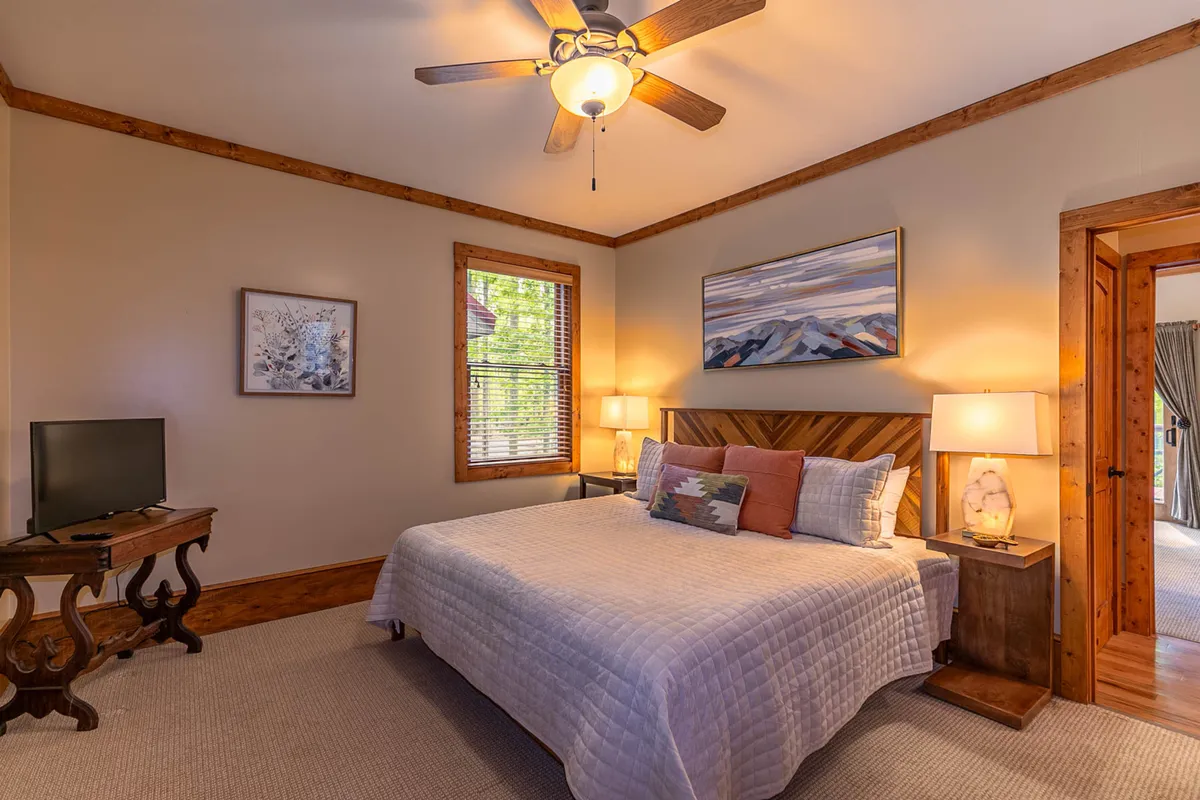 An inviting bedroom with a comfortable bed, tasteful artwork, nightstands, and a bright window. The space is bathed in natural light, evoking a peaceful start to the day.