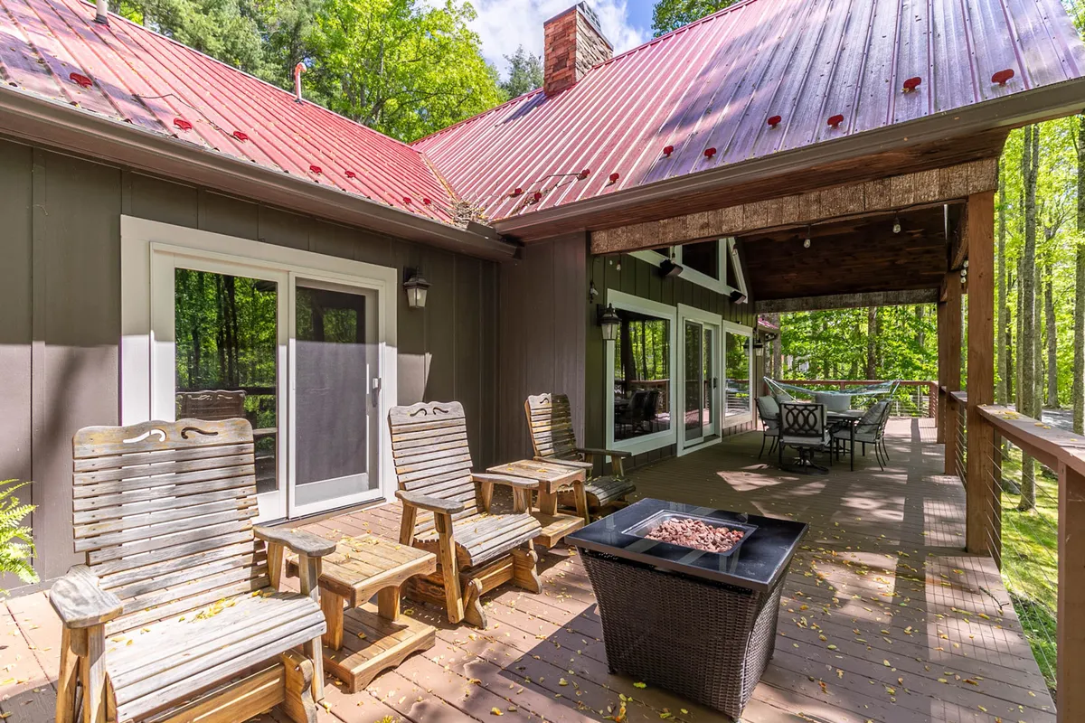 A covered porch area with wooden chairs grouped around a fire pit, large windows, and views of the outdoors. The setting feels social and welcoming, ideal for both family gatherings and spending time outside with pets.
