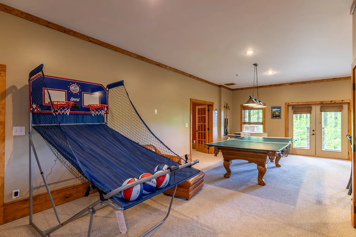 A dedicated recreation space with a basketball arcade game, a sleek pool table, and double doors that open to the outside. The room is bathed in natural light, inviting both active play and relaxed socializing with friends and family.