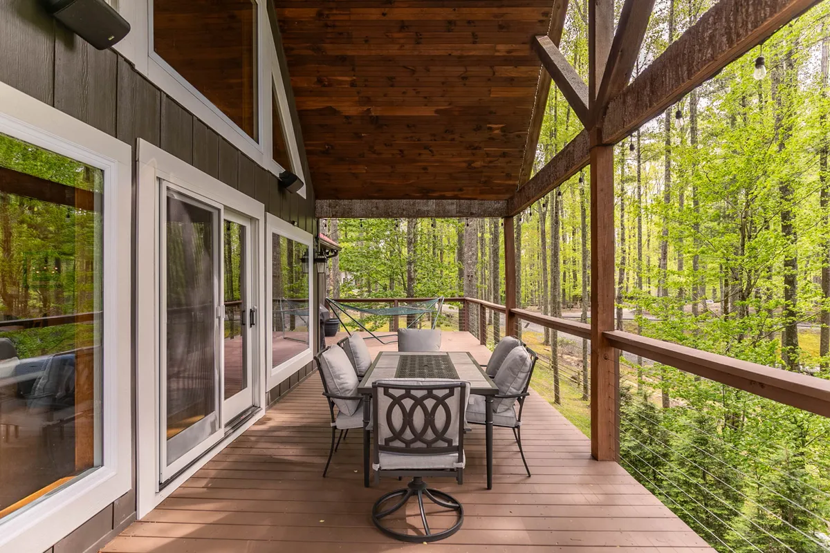An inviting wooden deck is surrounded by trees, with a dining table set for outdoor meals and glass doors connecting to the interior. The atmosphere is serene and perfect for family gatherings or relaxing after a day out.