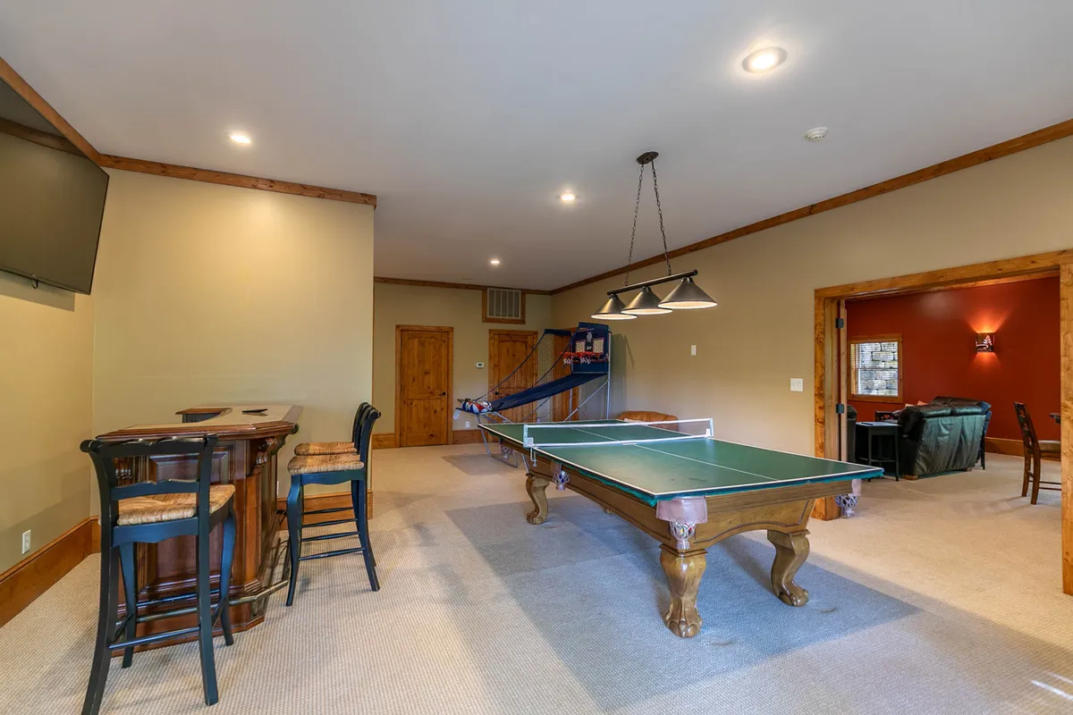 A casual and inviting interior game room featuring a ping pong table, bar area, and staircase. The space is set up for friendly matches and socializing, encapsulating the fun, active spirit of the property.
