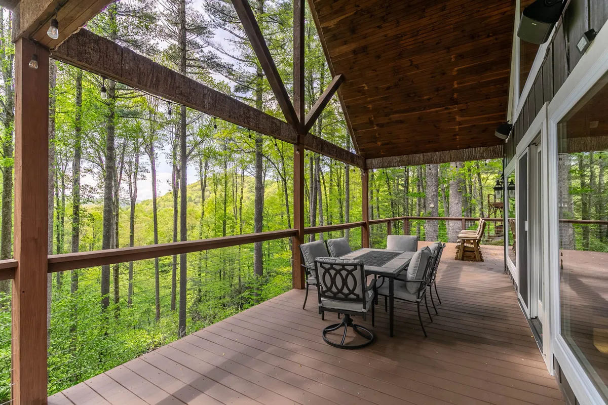 This image features a spacious wooden deck outfitted with a dining table set amidst lush green trees. The space is tranquil and designed for outdoor dining, relaxation, and gathering, making it ideal for enjoying morning coffee, sunset meals, or communal barbecues.