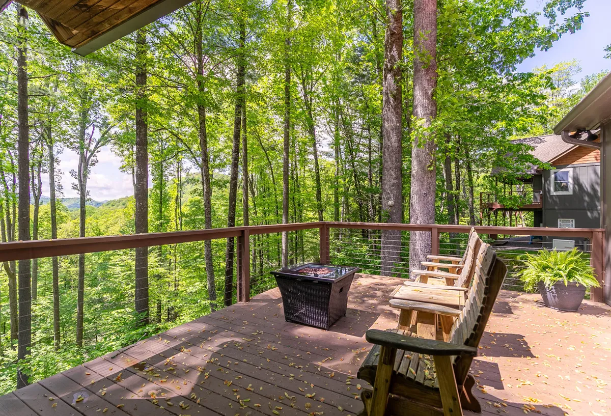A wooden deck with a comfortable seating area and a fire pit overlooks the surrounding trees. The setting is peaceful, inviting guests to relax, socialize, or stargaze in the evening.