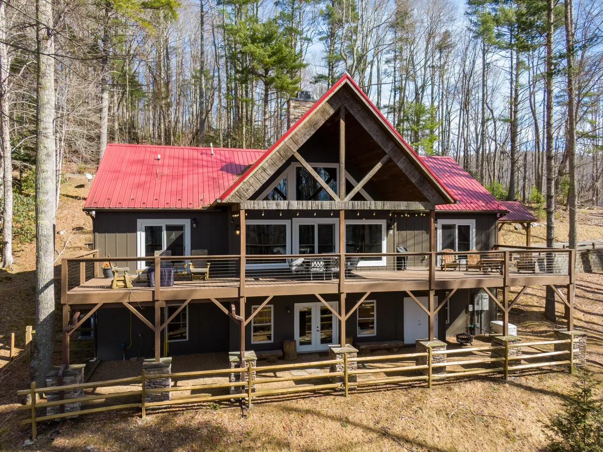 A spacious wooden deck with a red metal roof and large windows overlooks a verdant forest, inviting guests to gather outdoors. The deck is surrounded by lush trees, offering privacy and a sense of immersion in nature. This exterior scene captures the tranquil beauty of the lodge’s setting, while the deck itself is large enough for group dining or socializing under the open sky.