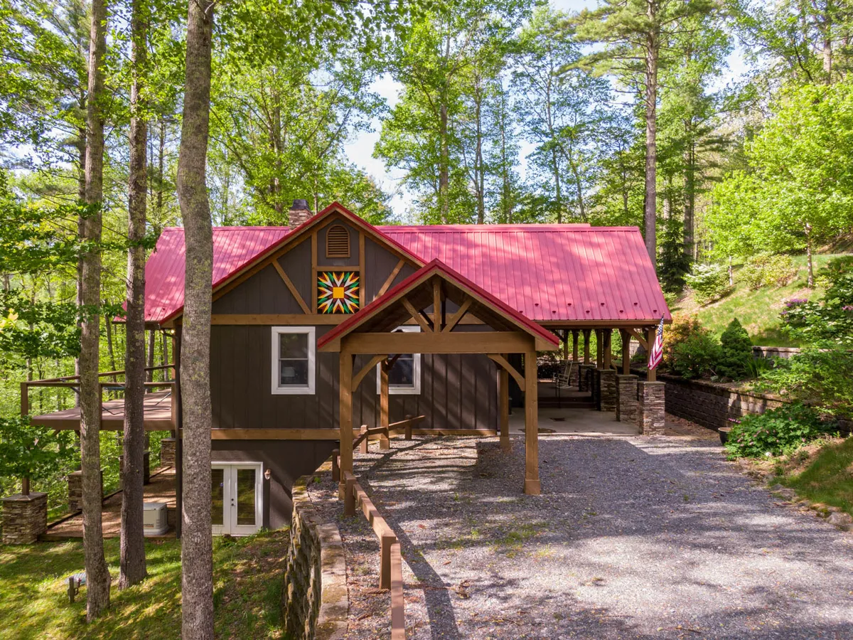 The exterior of the lodge features a welcoming porch beneath a red metal roof, adorned with a colorful quilt square decoration. Surrounded by trees and set up for gatherings, the porch invites guests to celebrate holidays, share stories, and enjoy the outdoors together.