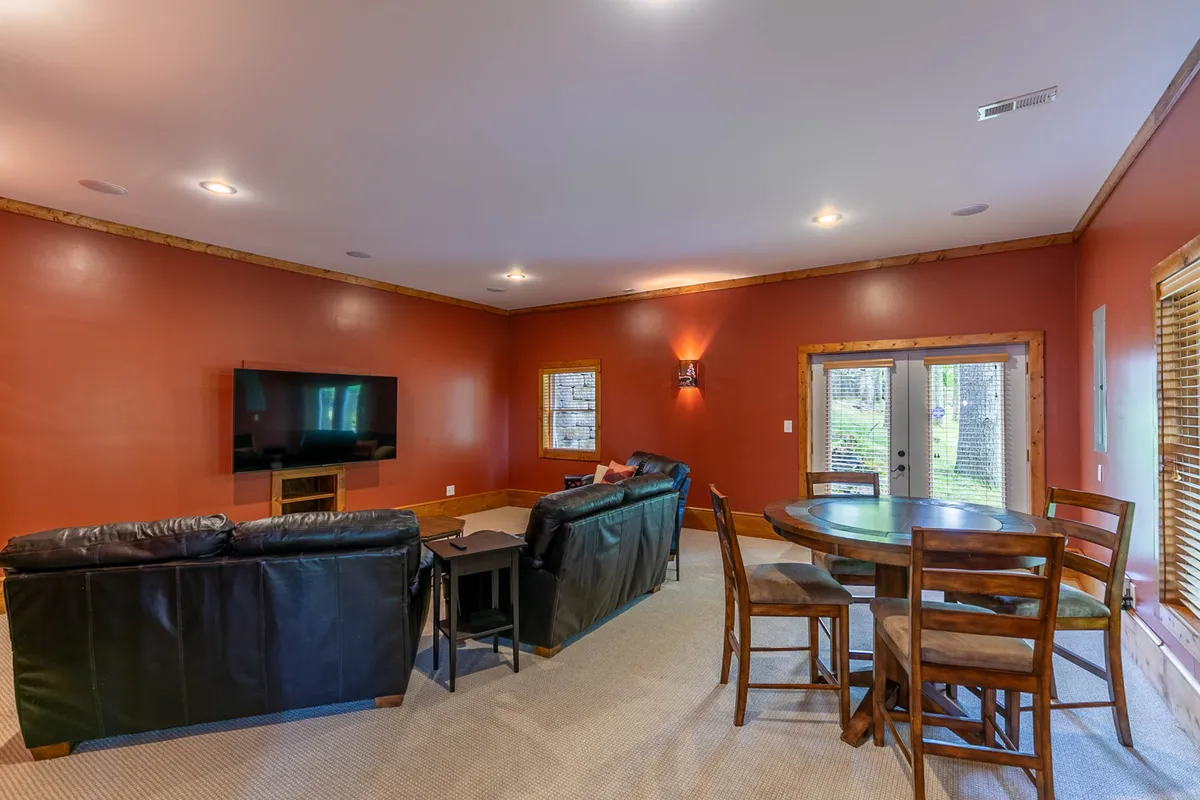 A spacious lower-level family room boasting large, comfortable leather sofas, a flat-screen TV for movie nights, a roomy dining table for board games, and panoramic windows that let in ample natural light. The atmosphere is relaxed and inviting, perfect for unwinding after a day of mountain adventures.
